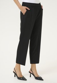 Pantaloni neri su misura con una vestibilità slim, dotati di tasche laterali e una texture liscia. Abbinati a décolleté nere con punta.