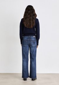 Suéter de punto azul marino con dobladillo acanalado, combinado con vaqueros de mezclilla azul de pierna ancha, que cuentan con cinco bolsillos y costuras en contraste en la parte trasera.