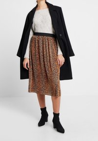 Falda de estampado de leopardo hecha de tela con una cinturilla negra, combinada con un suéter gris texturizado y un abrigo largo negro, llevada con botas negras hasta el tobillo.