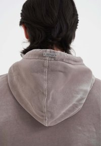 Felpa con cappuccio in tessuto grigio chiaro dal tocco morbido. Presenta una cucitura e un'etichetta metallica sul retro del collo.