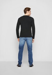 Schwarzes Langarmoberteil, kombiniert mit hellblauen Jeans. Das Oberteil hat einen runden Ausschnitt; die Jeans sind im klassischen Design mit Gesäßtaschen.
