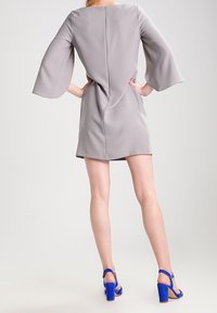 Grå kort klänning med volangärmar, dragkedja i ryggen och en figurnära silhuett. Matchad med blå mocka blockklackssandaler.