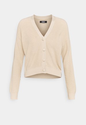 Cardigan court beige à manches longues, col en V, poignets et ourlet côtelés, avec quatre grands boutons recouverts sur le devant.
