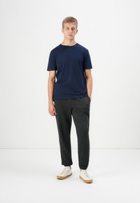 T-shirt à col rond marine, pantalon de survêtement gris avec des chevilles resserrées, et baskets blanches avec des semelles beiges. Texture de tissu lisse.