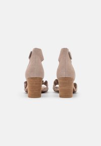 Beżowe zamszowe sandały na obcasie z okrągłym nosem, z małym wycięciem z tyłu i teksturowanym brązowym słupkiem.