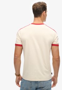 Cremefarvet t-shirt med korte ærmer og rød krave og ærmekanter, der har en glat tekstur og en tætsiddende pasform. Bagvisning vist.