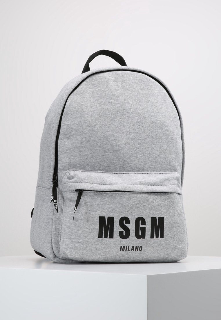 Sac à dos en tissu gris clair avec des détails de fermeture éclair noirs et "MSGM MILANO" imprimé en lettres noires en gras sur la poche avant.