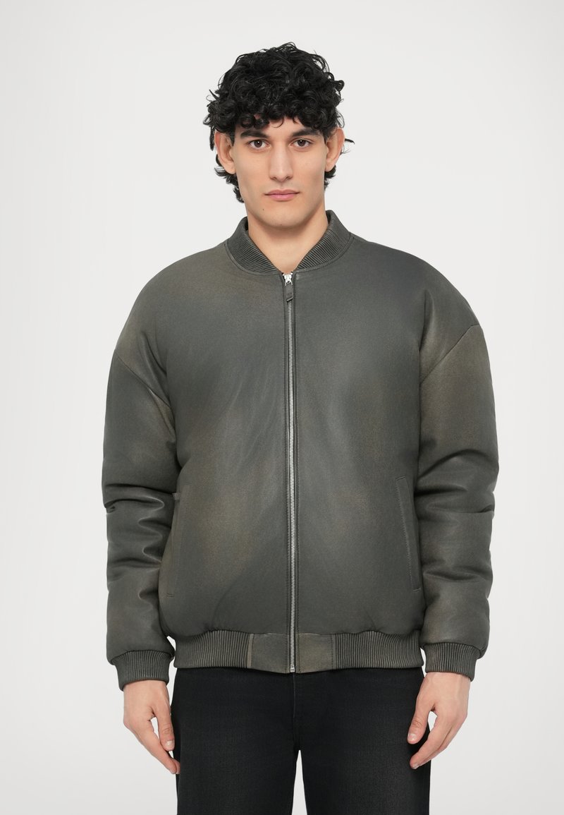 Tamsiai pilka bombonešio striukė iš netikros odos su ribiniais rankogaliais ir apykakle, priekyje su užtrauktuku ir šoninėmis kišenėmis. Lygus, šiek tiek tekstūruotas paviršius.