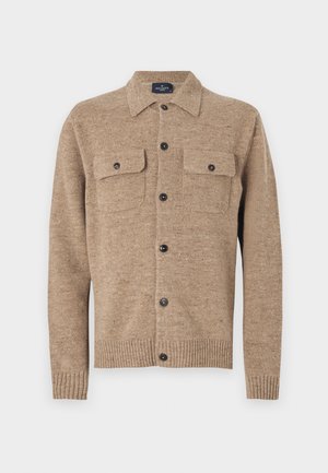 Brązowy kardigan wełniany z kołnierzykiem, dwoma kieszeniami na piersi i czarnymi guzikami. Ma prążkowane mankiety i dół. Teksturowany materiał z drobnymi włóknami.