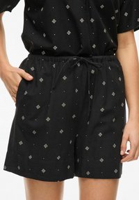 Pantaloni corti neri con vita elastica, dotati di cordino, e un motivo di forme a diamante bianche e piccoli punti in tutto il tessuto.