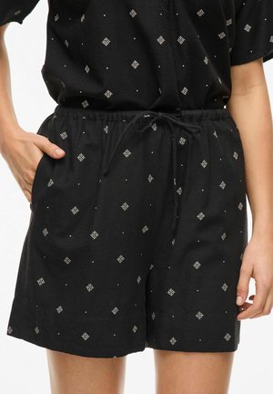 Zwarte shorts met een elastische tailleband, voorzien van een trekkoord, en een patroon van witte diamantvormen en kleine stippen overal.