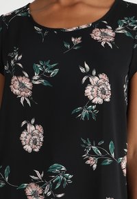 Blusa negra con un diseño floral que presenta flores rosas y hojas verdes. Tejido suave, mangas cortas y escote redondeado.