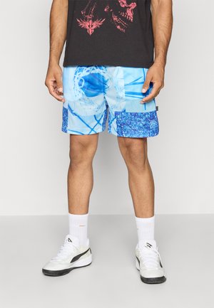 Lysblå mesh-shorts med geometriske mønstre i forskellige nuancer af blå. Har en ensfarvet blå lap på det ene ben. Båret med hvide sokker og sko.