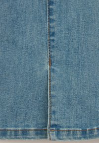 Ljusblå denimtyg med en synlig söm och kontrasterande bruna sömmar, med en något strukturerad yta och en rak passform.