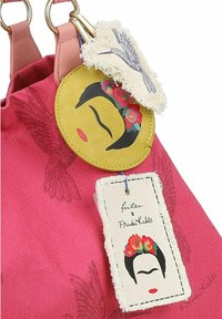 Roze stoffen tas met twee gouden hardware ringen, met drie decoratieve labels: een bloemrijke portret van Frida Kahlo, een franjes label in het wit, en een vogelontwerp.