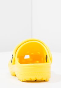 Sabots jaunes en plastique léger, dotés d'une sangle à l'arrière, d'aérations circulaires et d'une semelle texturée pour une bonne adhérence. Aucun motif ou accent supplémentaire.