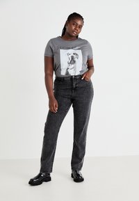 T-shirt graphique gris avec un motif de chien et le texte "COOL GIRL", associé à un jean noir avec des embellissements cloutés et des bottes noires épaisses.