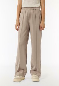 Light beige wide-leg trousers with an elastic waistband, soft texture, and side buttons at the hem, paired with cream sneakers.