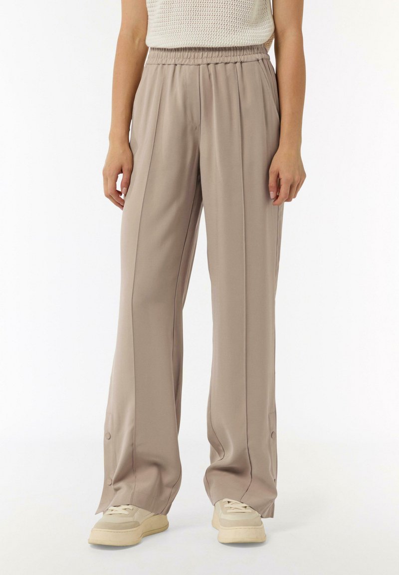 Light beige wide-leg trousers with an elastic waistband, soft texture, and side buttons at the hem, paired with cream sneakers.
