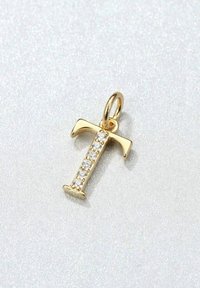 Colgante en forma de letra "T" dorada adornado con cinco cristales transparentes, con un lazo para ser colocado en cadenas o pendientes, sobre un fondo claro y texturizado.