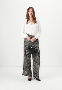 Black and white patterned wide-leg pants, white long-sleeve blouse, and black handbag. Pointed black heels complete the look.