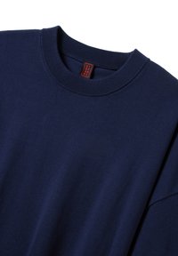 Sweatshirt bleu marine à col ras du cou avec des bords côtes aux col et aux manches, texture douce, et une petite étiquette rouge portant le nom de la marque à l'intérieur du cou.