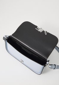 Borsa a tracolla con parte superiore in pelle nera e base in pelle azzurra chiara, dotata di hardware in argento e chiusura a scatto. Tasca interna visibile.