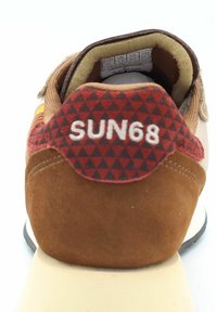 Sneaker in suede marrone con un tallone a tab in tessuto a diamante rosso e nero etichettato "SUN68". Presenta una linguetta beige e una suola bianca.