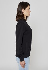 Sweat-shirt noir à col montant et poches latérales, fabriqué en tissu doux. Présente une coupe ajustée avec des poignets et un ourlet côtelés.