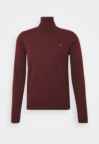 Bordeauxroter Rollkragenpullover aus feinem Strickgewebe. Mit langen Ärmeln und einem kleinen goldenen Logo auf der Brust. Glatte, weiche Textur.