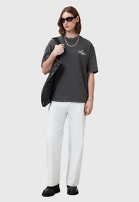 T-shirt en coton gris oversize avec un graphique sur le devant ; associé à un pantalon droit blanc et des chaussures en cuir noires ; portant un sac en cuir noir.