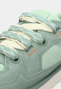 Baskets en daim vert avec des lacets texturés menthe et des accents vert clair. Présentent des coutures orange contrastantes et des œillets ronds.