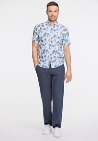 Camicia a maniche corte di colore azzurro con motivo floreale, abbinata a pantaloni blu scuro e sneakers bianche. Presenta un colletto button-down e una vestibilità morbida.