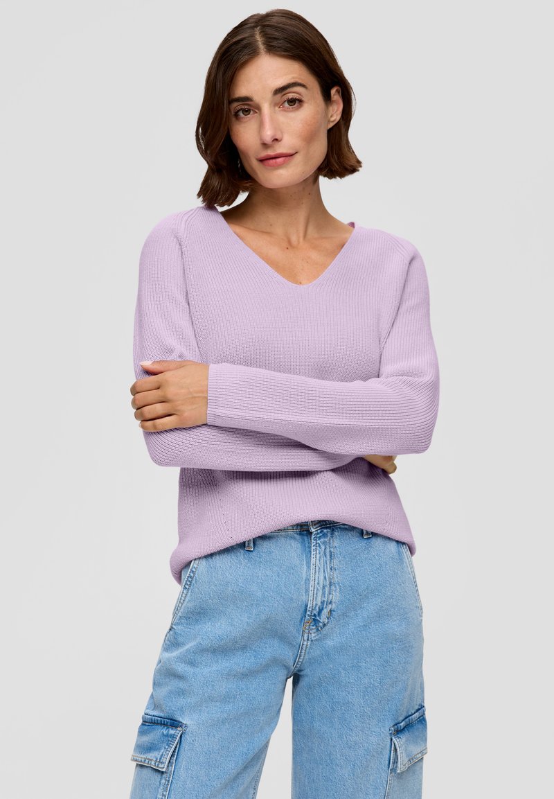 Lichtpaarse ribtrui met een V-hals en lange mouwen, gecombineerd met lichtblauwe cargo jeans met zijzakken.