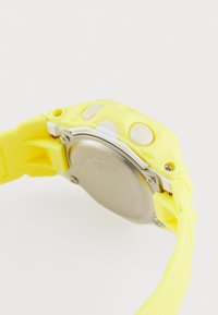Yellow silicone watch with a round silver metal back, white push buttons, and unique textured band. Features a modern and chunky design.