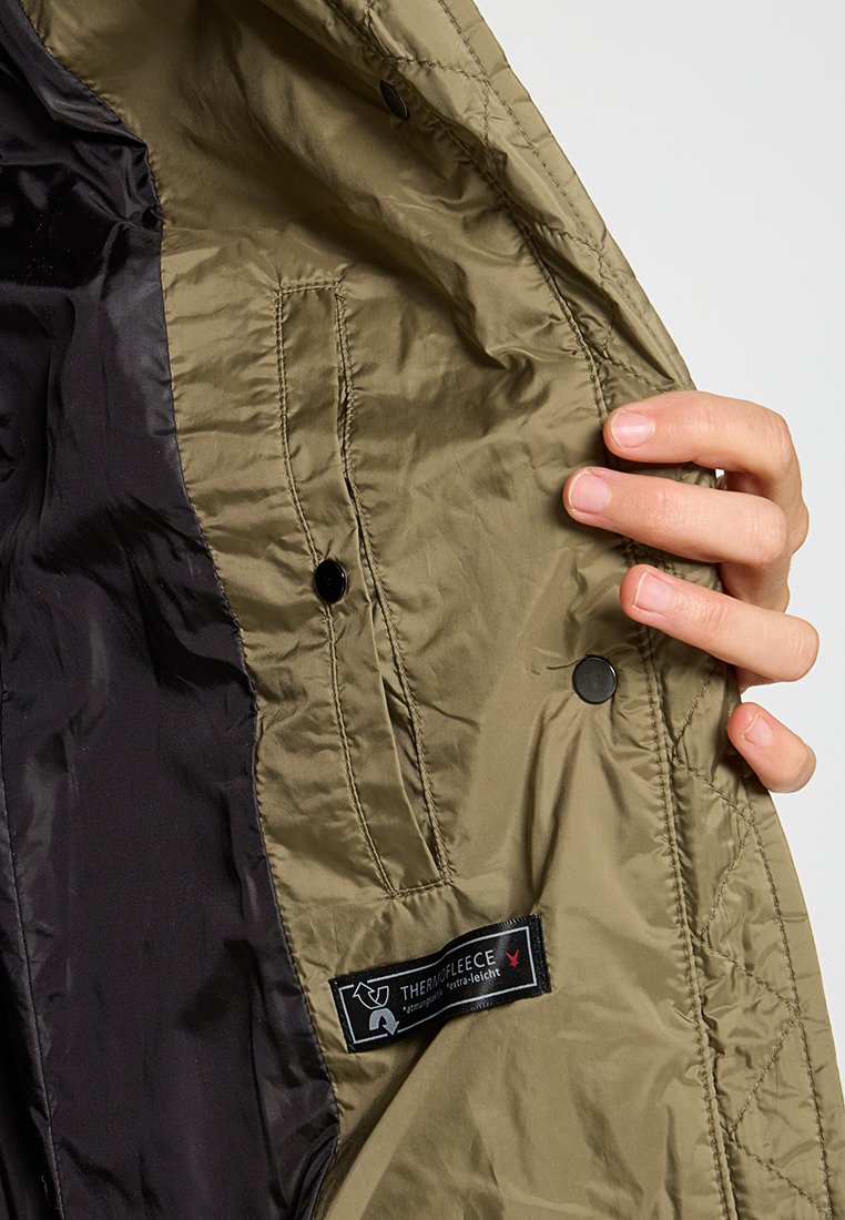Interno di giacca isolante khaki con rivestimento nero, con etichetta "THERMOFLEECE" e due bottoni a pressione neri.