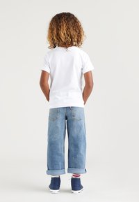 Vit kortärmad t-shirt, blå uppvikta denimjeans, marinblå högstövliga skor, röd- och vitrandiga strumpor, sedd bakifrån.