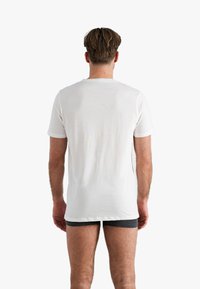 Witte katoenen t-shirt met korte mouwen, ronde hals en een rechte snit, van achteren weergegeven. Glad textuur, minimale details.