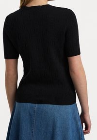 Černý pletený top s krátkým rukávem, který má jemný strukturovaný vzor a vroubkovaný lem. Kombinovaný s modrou džínovou sukní.