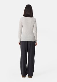 Maglione aderente grigio chiaro con maniche lunghe, realizzato in materiale morbido, abbinato a pantaloni neri larghi, visto da dietro.