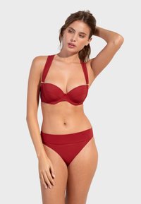Crveni bikini set koji se sastoji od oblikovanog topa s žicom i širokim naramenicama te zlatnim detaljima, uparen s srednje visokim, glatkim donjim dijelom.