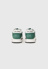 Zapatillas de ante verde con acentos en blanco, que cuentan con una suela acolchada y partes texturizadas en el talón, mostrando la marca "CONVERSE".