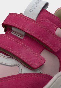 Κοντινή λήψη ενός ροζ και άσπρου αθλητικού παπουτσιού με δύο ρυθμιζόμενους ιμάντες Velcro και ορατές ραφές.