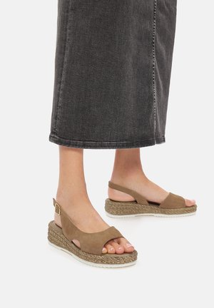 Sandalias de cuña de ante marrón con tira al talón, puntera abierta y detalles de rafia trenzada en la suela. El diseño incluye acentos recortados.