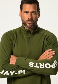Maglione verde a maniche lunghe con colletto alto e mezza zip, caratterizzato da testo stampato bianco su entrambe le maniche. Texture liscia, vestibilità atletica.