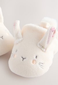 Witte pluche pantoffels met konijnendesign, met geborduurde gezichtsdetails, zachte textuur en opstaande oren met accenten van roze stof.