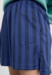 Sötétkék sportnadrág, különböző árnyalatú függőleges csíkokkal. Gumírozott derék és kis fekete Nike logó elöl. Könnyű anyag.
