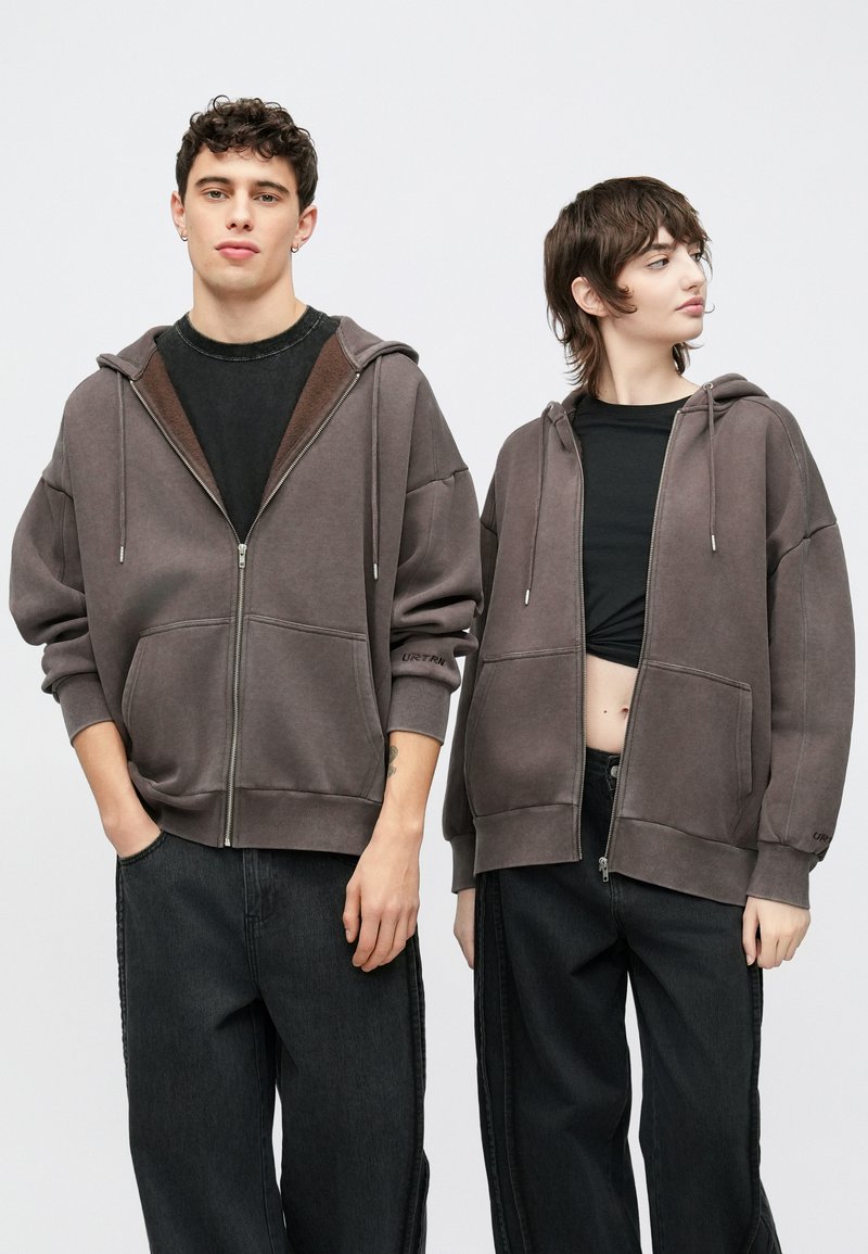 Δύο άτομα φορούν φαρδιές φούτερ με φερμουάρ σε απαλό γκρι χρώμα. Το ύφασμα είναι μαλακό με εμφανείς ραφές και μεγάλες μπροστινές τσέπες.