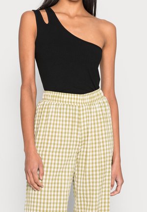 Czarny prążkowany top na jedno ramię w zestawieniu z zielonymi i białymi spodniami w kratę typu wide-leg, z elastycznym pasem.