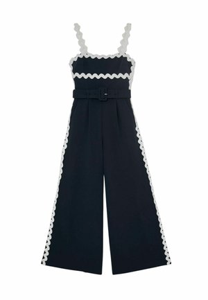 Salopetă largă bleumarin cu margine ondulată albă, bretele fără mâneci, decolteu pătrat și curea asortată în talie.